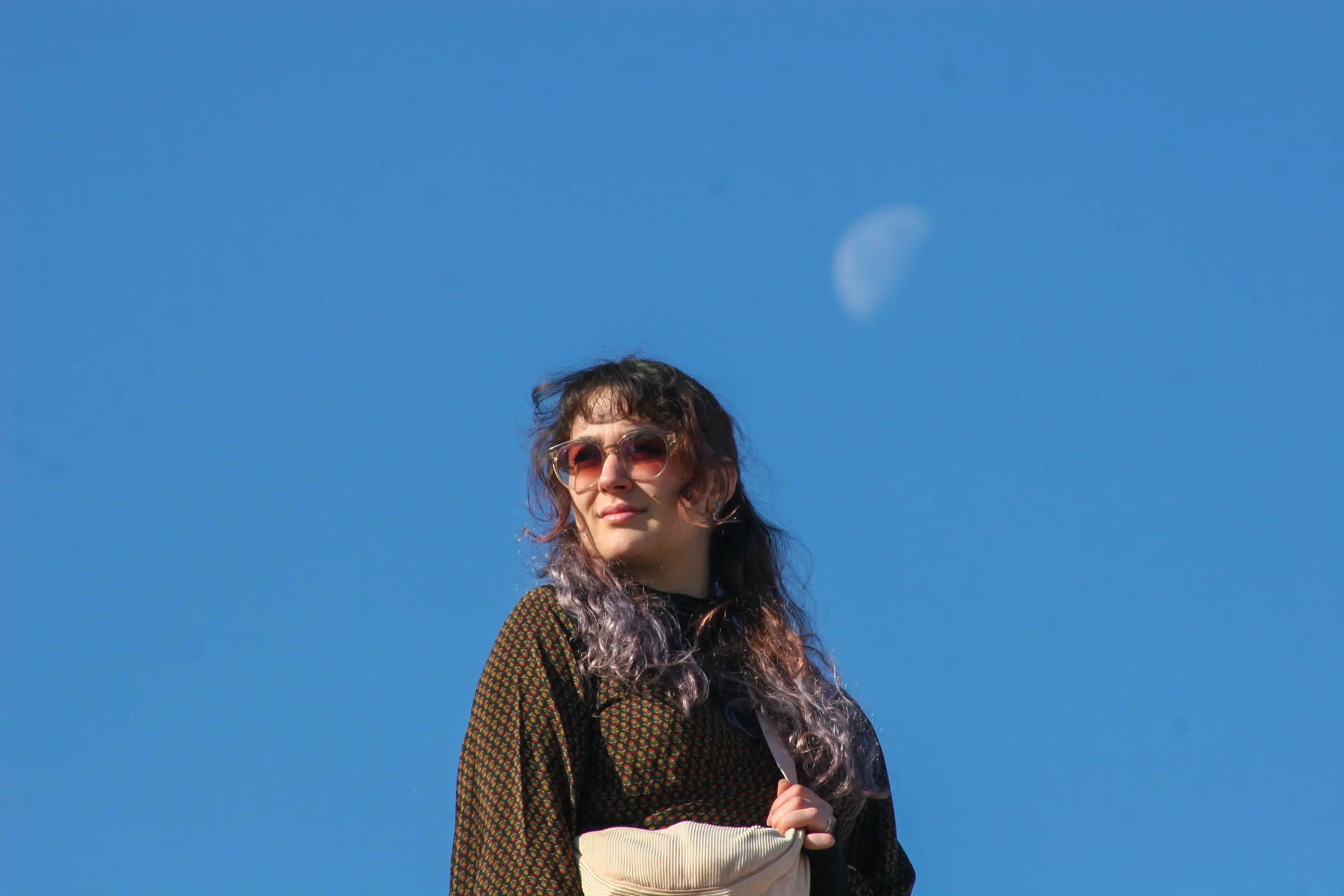 A portrait photo with a distant moon on a clear blue sky.